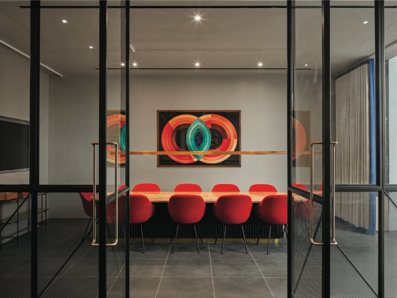 Glass-walled meeting room with red chairs around a long table