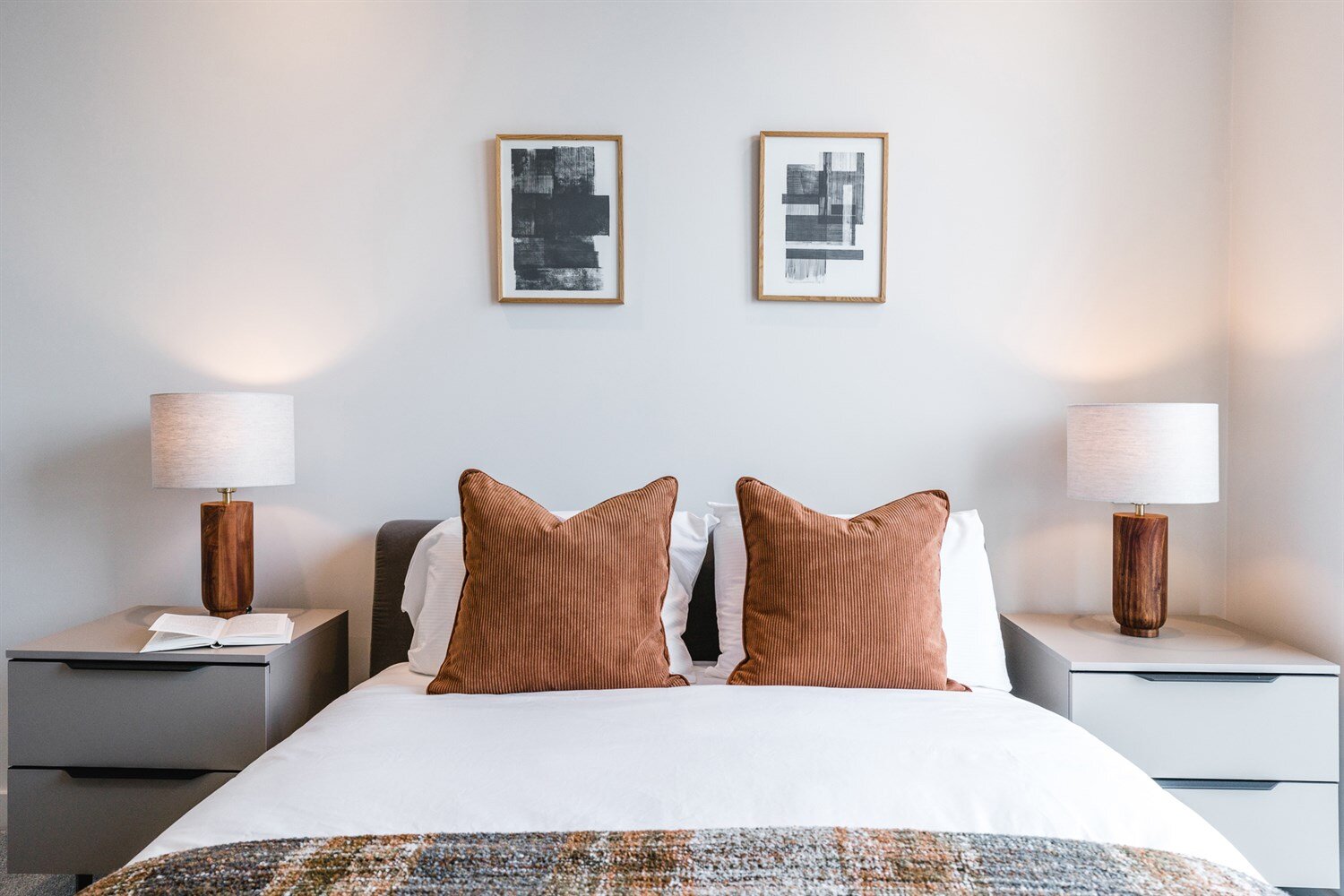 Rust corduroy cushions on a made bed between two wooden lamps