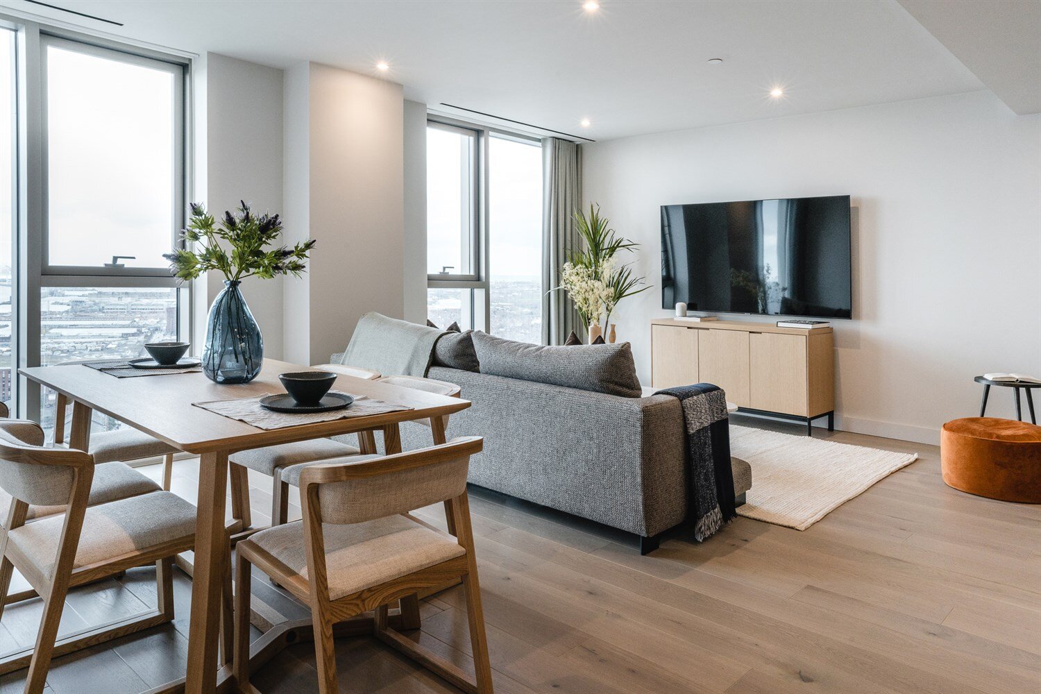 Living and dining room with oak floors, a grey sofa and floor-to-ceiling windows over the docks
