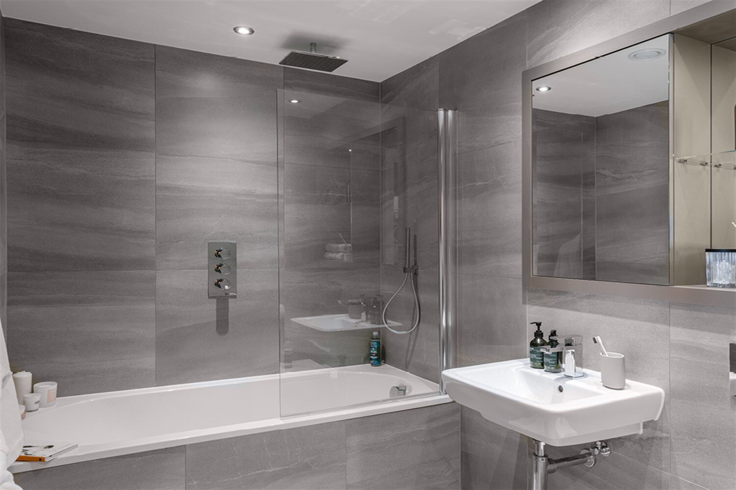 Bathroom with a bath and shower, large grey tiles and a wide mirror, at The Mercian, Birmingham
