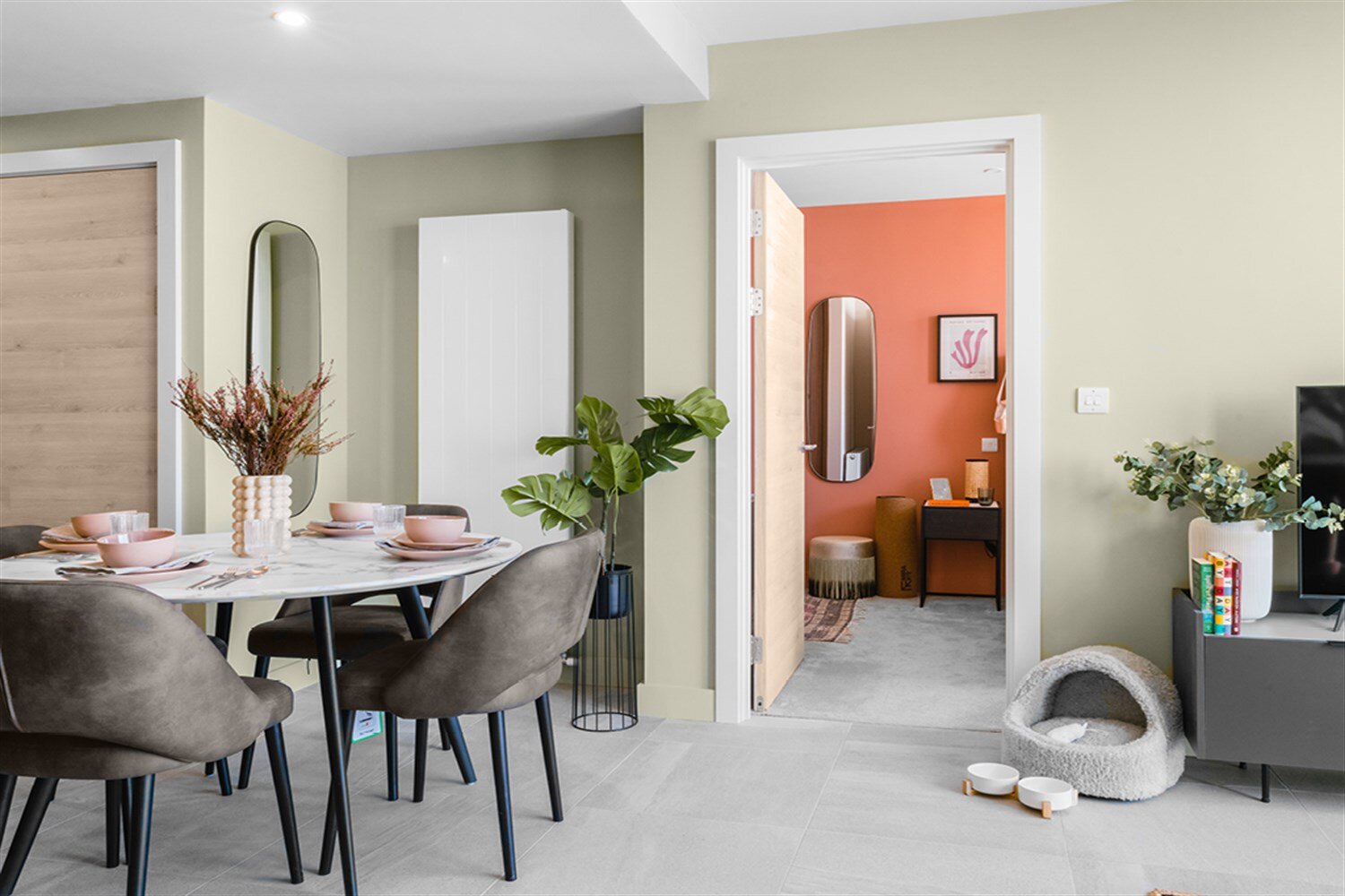 Round marble dining table between sage walls, with a coral bedroom through the door, at The Mercian, Birmingham