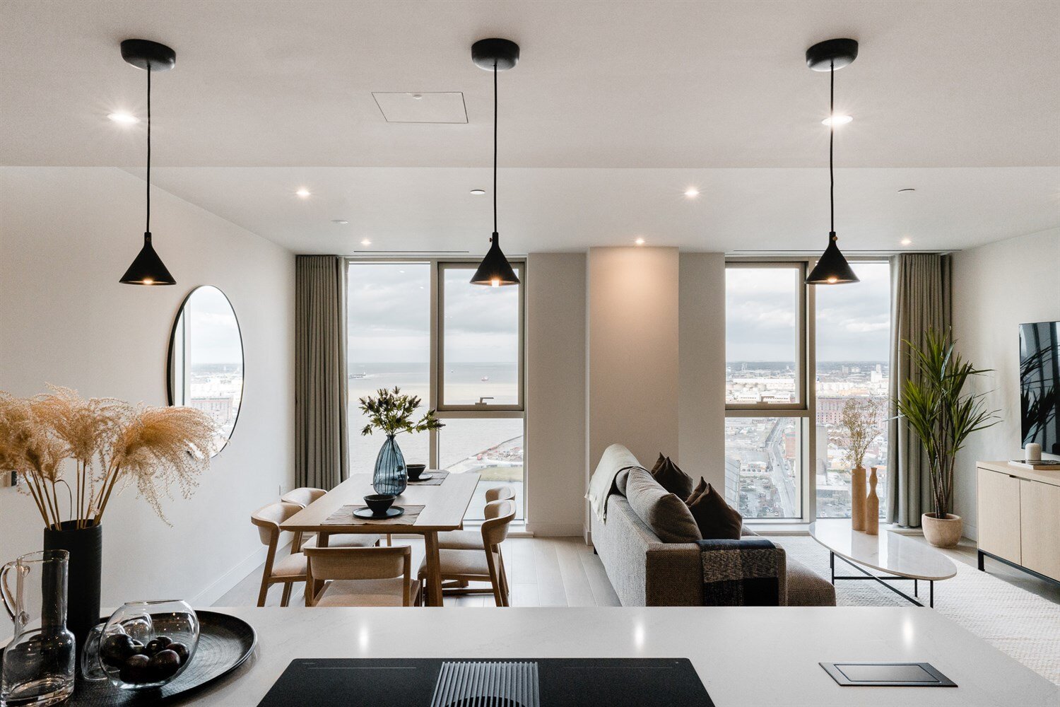 Open-plan living room beneath black pendant lights, with the River Mersey beyond two tall windows