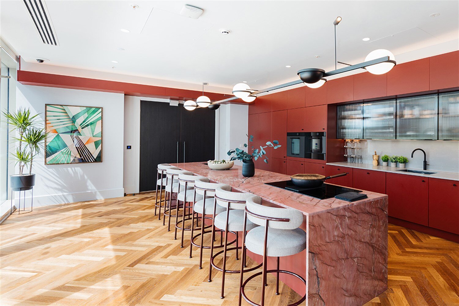 Residents' kitchen with a pink marble island, red cabinetry and globe pendant lights, at The Mercian, Birmingham