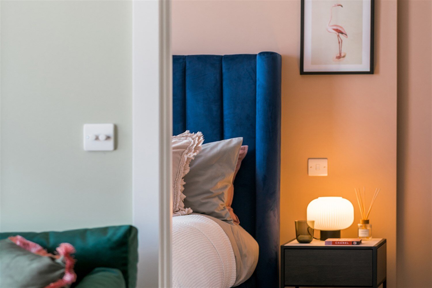Glowing bedside lamp beside a navy velvet headboard and a coral wall