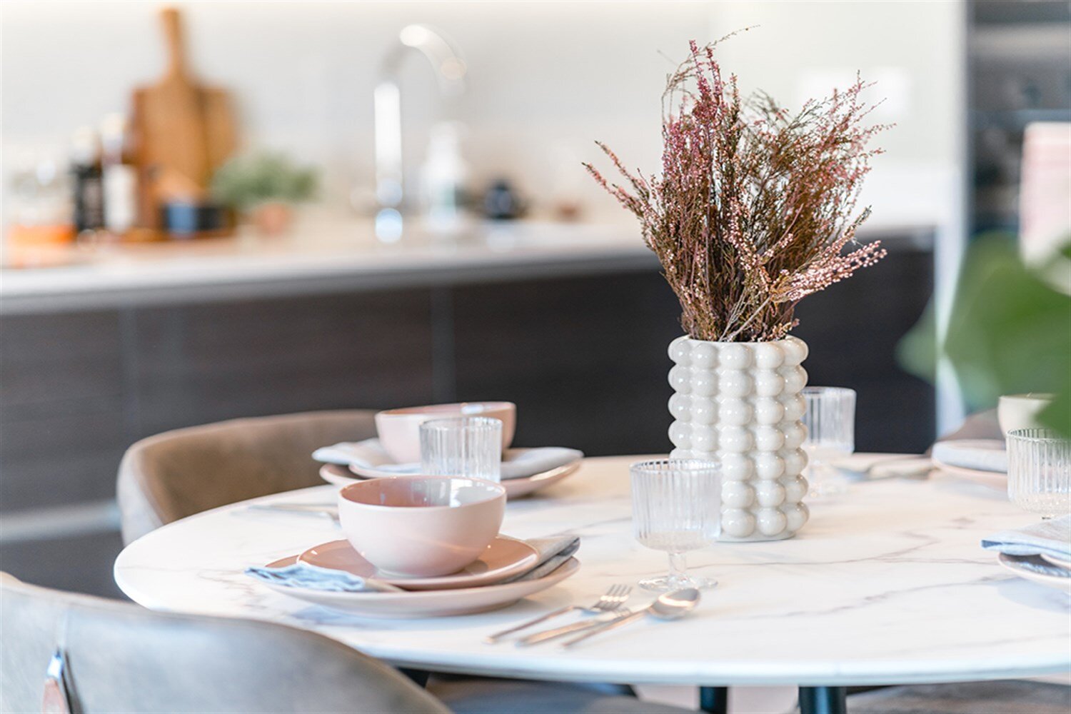 Marble table laid with blush plates beside a vase of dried flowers