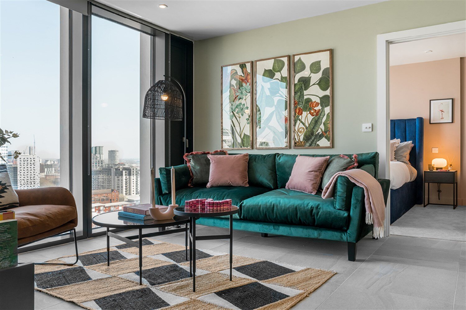 Living room with a green velvet sofa, botanical prints and floor-to-ceiling windows over the city