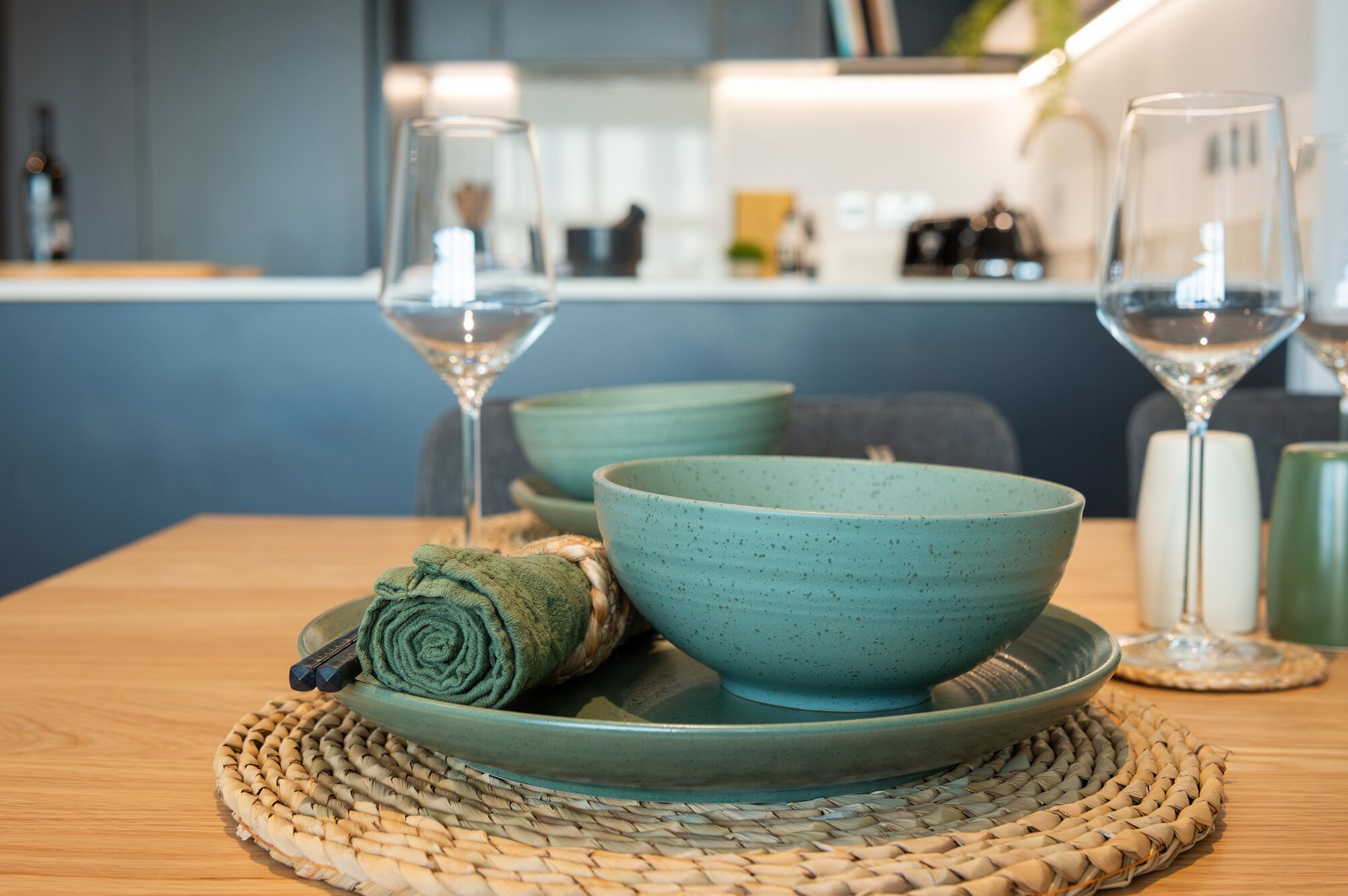 Teal bowls and wine glasses on a woven placemat at the dining table