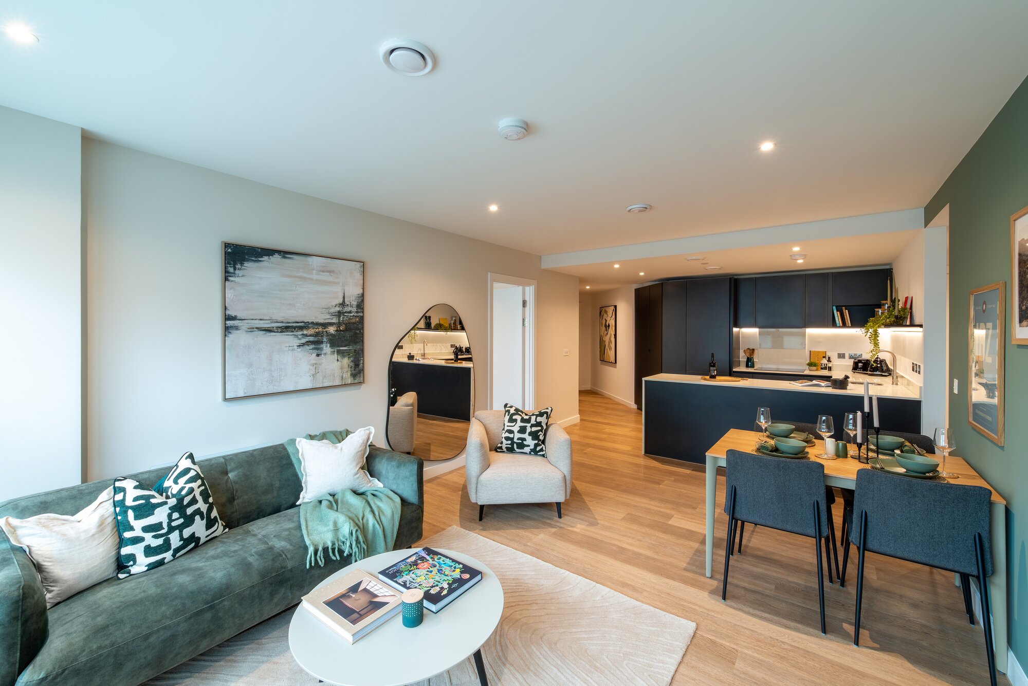 Living room with a green sofa, a round coffee table and the kitchen beyond