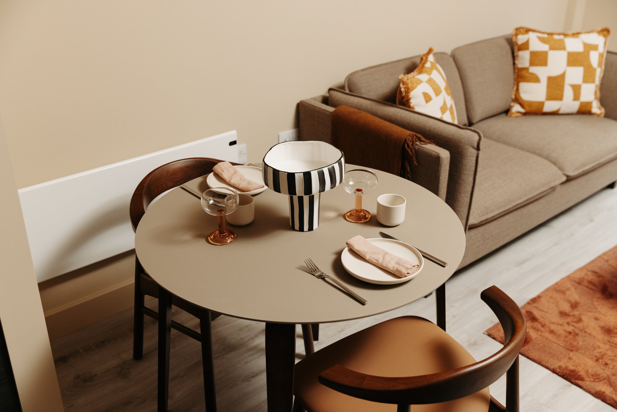 Round dining table laid for two beside a sofa with checked cushions