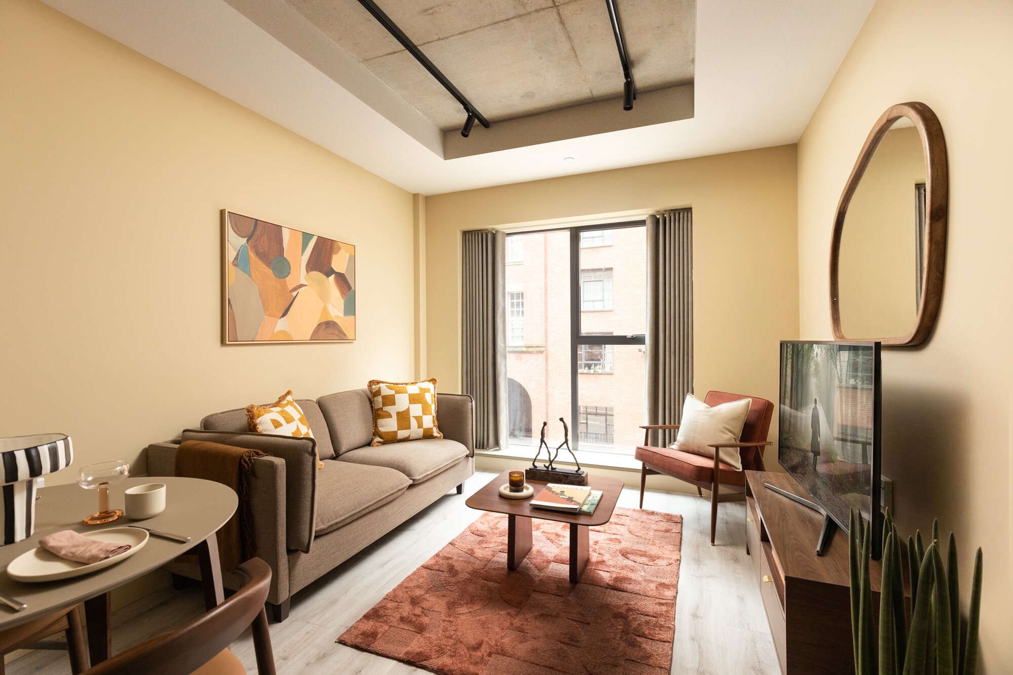 Living room with a sofa, mustard checked cushions, a rust rug and a sculptural mirror