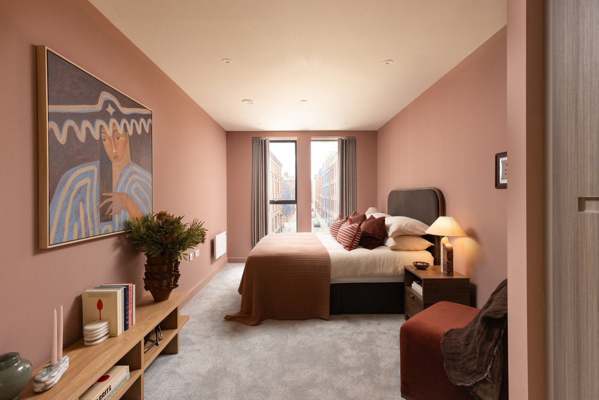 Bedroom with blush walls, a large portrait painting and a velvet chair