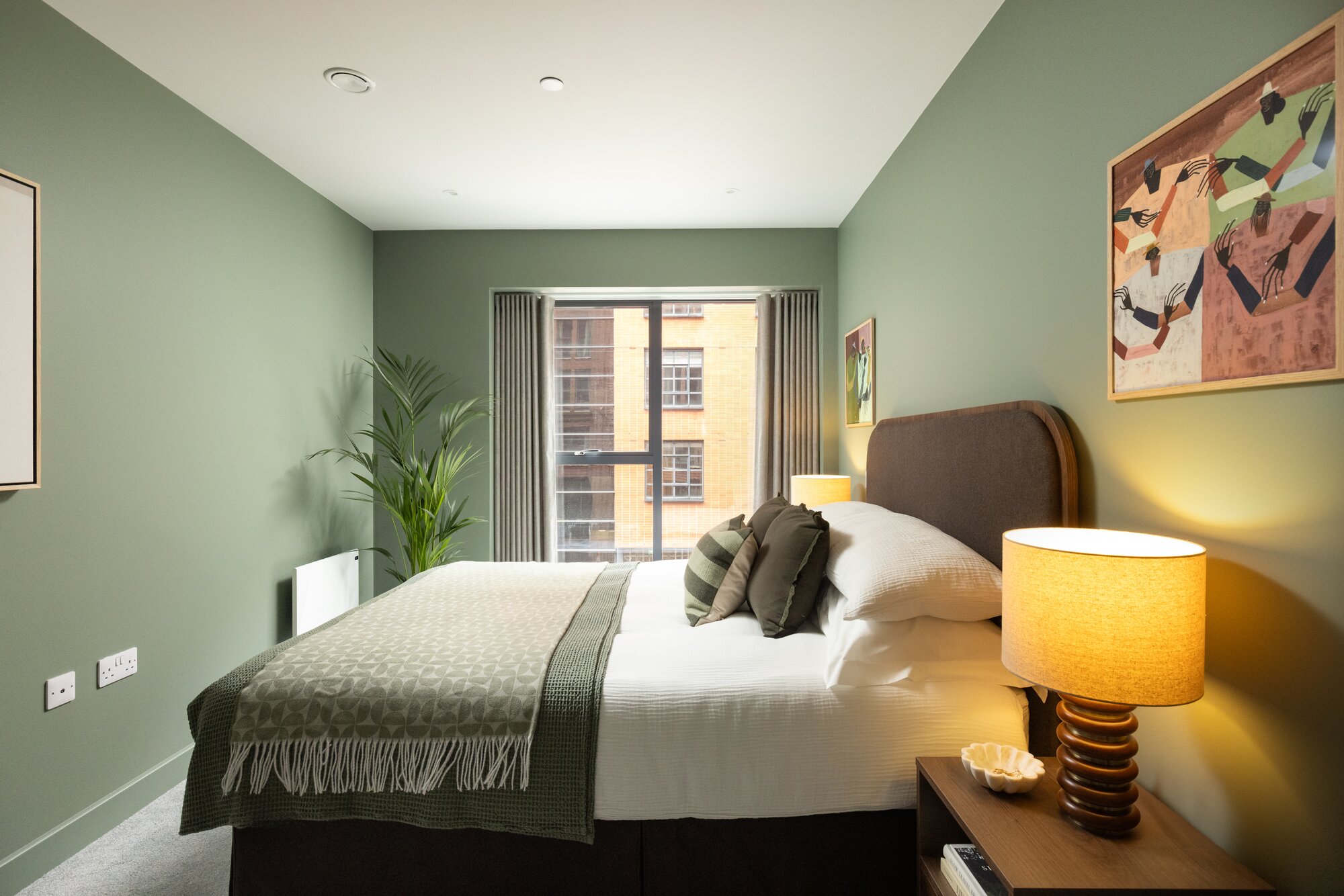 Bedroom with sage walls, a woven throw and a ribbed lamp glowing at the bedside