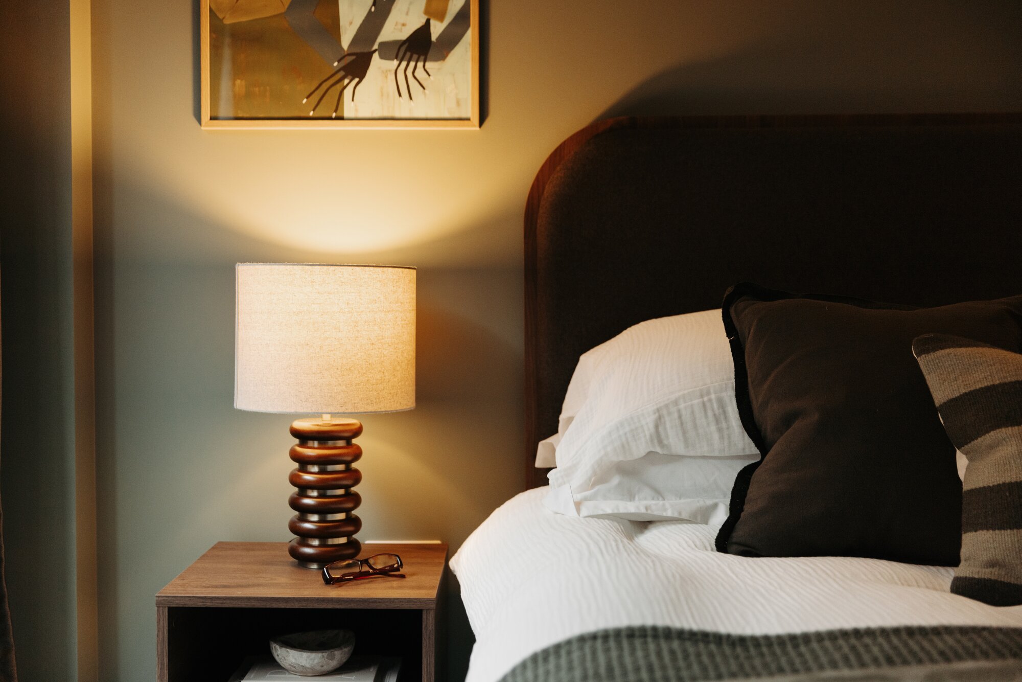 Ribbed bedside lamp glowing beside a dark upholstered headboard